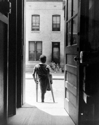 Washington, D.C. Young boy standing in the doorway of his home on Seaton Road in the northwest section. His leg was cut off by a streetcar while he was playing in the street