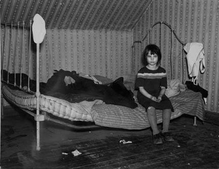 One of Edgar Allen's children sitting on the bed in the house on his farm. There are no sheets, pillowcases, or pillows (other than makeshift) in use. Bedding usually consists of castoff rags and a few old blankets. Near Milford, Iowa. They are helped by the Resettlement Administration