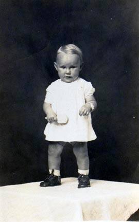 Untitled (toddler girl standing and holding rattle)