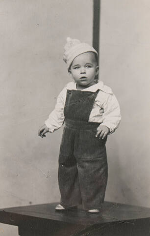 Untitled (small boy in overalls and cap standing on table)