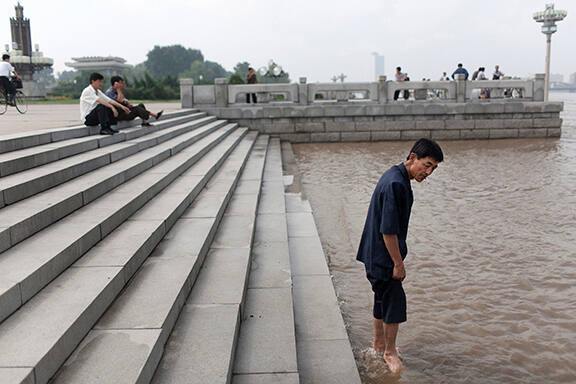 A man wades into the Tae Dong river where banks are flooded