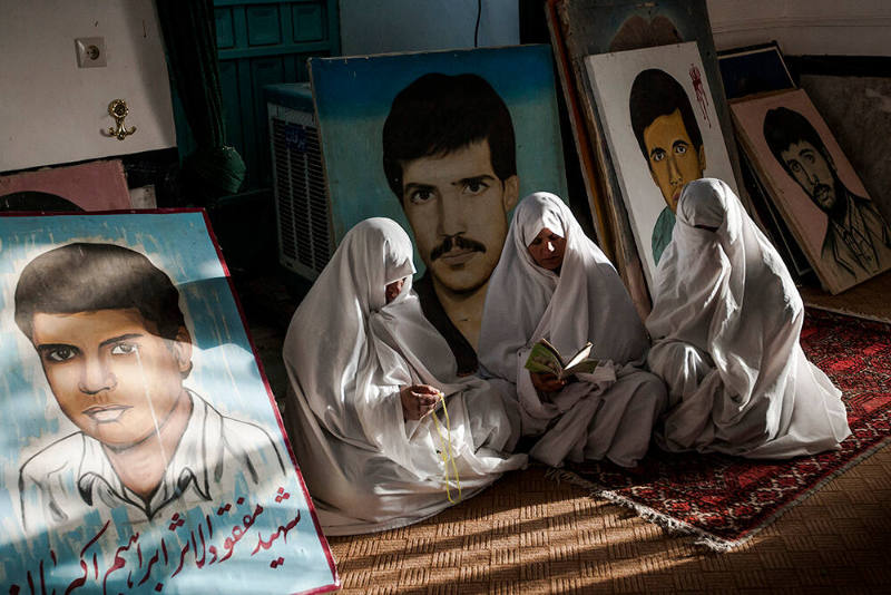 Varzaneh, Isfahan Province, Iran. The mother of martyrs, those who died in the Iran-Iraq war, praying at the graves of their sons and surrounded by their portraits.