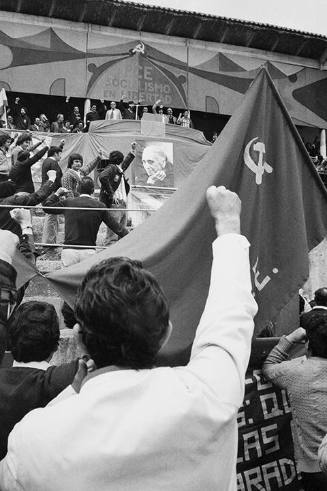 Crowd member raising fist in front of communist flag during Communist meeting in bullring, Oviedo, Spain