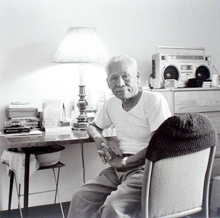 Man at desk with boom box and wash bowl, at the Harold Washington SRO, from the Edge of Shelter Project